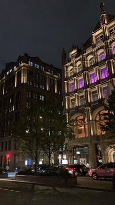 a city street at night with cars parked on the side and buildings lit up in purple lights