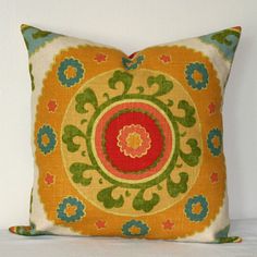 an orange and green decorative pillow on a white surface with a red flower in the center