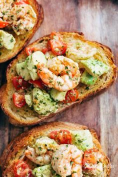 three pieces of bread with shrimp and vegetables on them sitting on top of a wooden table