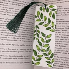 a bookmark with green leaves and tassels on top of an open book