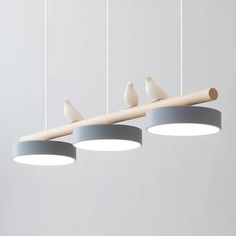 three birds are perched on the end of a light fixture that is suspended above two circular lights