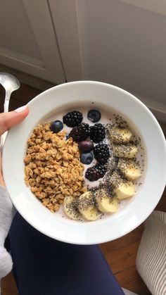 a person holding a bowl of oatmeal with bananas and blueberries