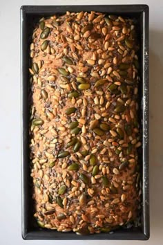 a loaf of bread covered in seeds and nuts on top of a baking pan,