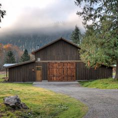 a wooden building sitting in the middle of a lush green field next to a forest