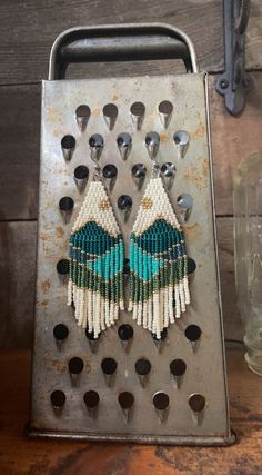 a pair of earrings made out of seed beads on a metal tray with spoons