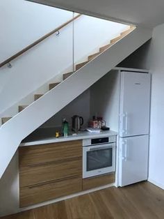 an empty kitchen with stairs leading up to the top floor and below it is a white refrigerator