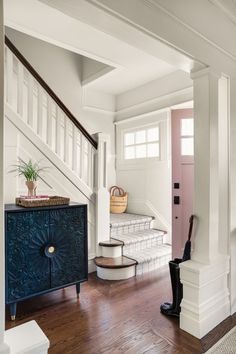 an entryway with white walls, wood floors and a blue cabinet in the center