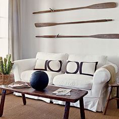 a living room with white couches and wooden paddles on the wall above them