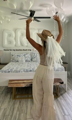 a woman in white jumpsuits and hat holding up some balloons above her head