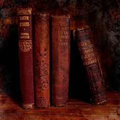 three old books sitting on top of a wooden shelf