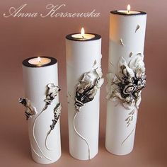 three white vases with flowers on them and candles in the middle one is lit