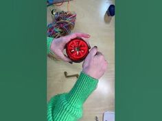 a person holding a red object in their hand on top of a wooden table next to yarn