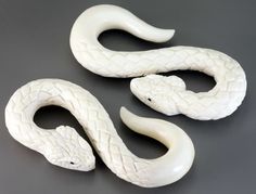 three white snake figurines sitting next to each other on a gray surface with black background