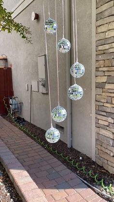 several disco ball lights hanging from the side of a building next to a brick walkway