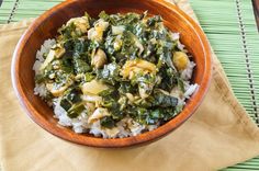 a wooden bowl filled with rice and greens on top of a green place mat next to a fork