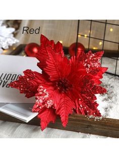 a red flower sitting on top of a table next to a white box filled with christmas decorations