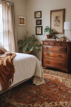 a bed sitting in a bedroom next to a wooden dresser and window filled with potted plants