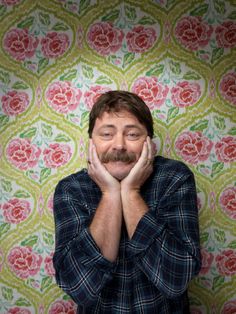 a man standing in front of a floral wallpaper with his hands on his face