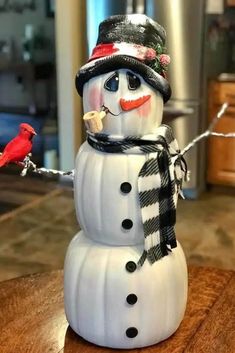 a snowman with a hat, scarf and bird on it's head sitting on a table