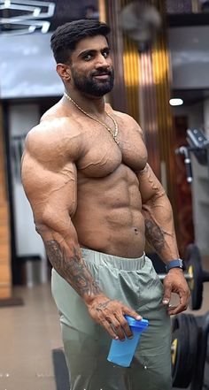 a shirtless man holding a water bottle and standing in front of a gym machine