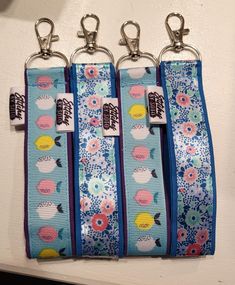 four lanyards are hanging from hooks on a white wall with blue and pink flowers