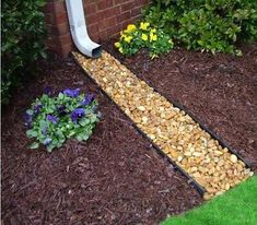 there is a garden bed with rocks and flowers in the front yard, next to a brick wall