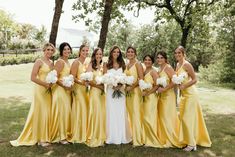 a group of women standing next to each other in front of trees and grass holding bouquets