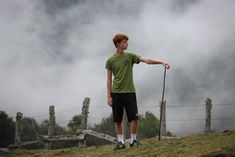 a young man standing on top of a grass covered hillside holding a stick in his hand