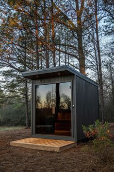 a small building in the middle of a forest with its doors open and trees around it