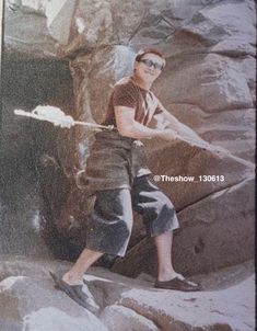 an old photo of a young boy holding a baseball bat in his right hand while standing on some rocks