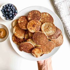 pancakes and blueberries on a white plate next to bowls of peanut butter and jelly