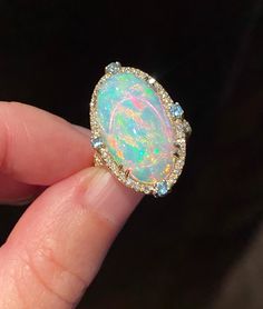 Gorgeous, mesmerizing Ethiopian opal cabochon of AAA quality is framed by dainty diamonds and four blue topazes on each side. The opal sparkles, showcasing streaks and circles of pink, deep blue colors, neon and yellow hues. A truly breathtaking stone! Four soft baby blue round faceted cut topazes add nice detail to the ring. In addition to the frame, diamonds are also placed on the split top part of the band adding more glamour and shine. Very beautiful and elegant ring! Stone: Ethiopian opal, Luxury Adjustable Opal Ring Gift, Luxury Ethiopian Opal Engagement Ring, Luxury Handmade Yellow Gold Opal Ring, Luxury Oval Cabochon Opal Ring For Formal Occasions, Luxury Cabochon Opal Ring For Engagement, Luxury Adjustable Opal Ring As Gift, Luxury Gold Opal Ring With Diamond Accents, Big Opal Ring, Elegant Opal Cabochon Ring