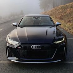 the front end of a black sports car driving down a road in foggy weather