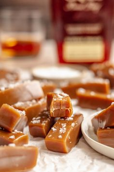 several pieces of caramel fudge on a white plate next to a glass bottle