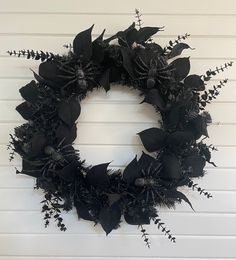 a black wreath hanging on the side of a white door with flowers and leaves around it