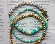 three beaded bracelets sitting on top of an open book with a cross charm