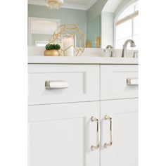 a bathroom with white cabinets and gold accents on the counter top, along with a candle holder