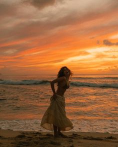 a woman standing on top of a sandy beach next to the ocean at sunset or dawn