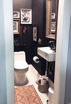 a white toilet sitting next to a sink in a bathroom under pictures on the wall