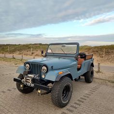 an old blue jeep is parked on the side of the road in front of some sand dunes