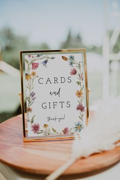 a card and gifts sign sitting on top of a wooden table next to a white feather