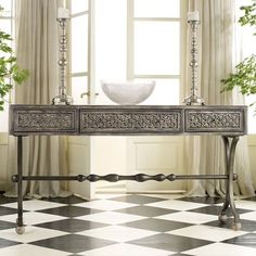 an ornate console table with two candles on it in front of a checkered floor