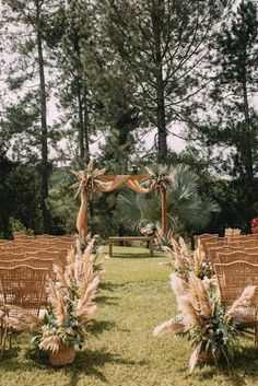 an outdoor ceremony set up with wicker chairs and floral arrangements on the grass, surrounded by tall pine trees