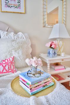 a stack of books sitting on top of a bed next to a vase with flowers