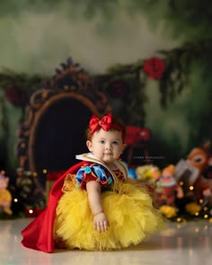 a baby girl dressed up as snow white in a yellow tutu and red cape