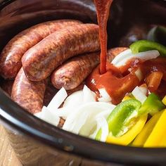 sausage being drizzled over vegetables in a crock pot on a wooden table