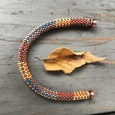 a beaded bracelet on a wooden surface with a leaf laying next to the beads