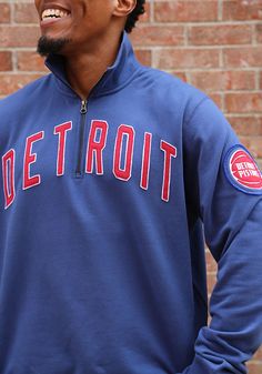 a man wearing a detroit red sox jacket and smiling at the camera while standing in front of a brick wall