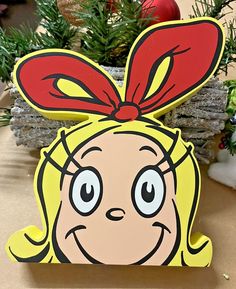 a cardboard cutout of a cartoon character with a red bow on her head, sitting in front of a christmas tree