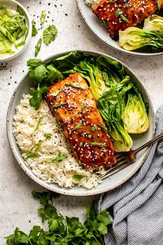 two plates with salmon, rice and vegetables on them next to some chopsticks